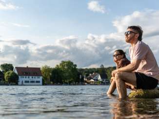 Two people are sitting on large rocks in the Rhine, cooling their feet in the water.