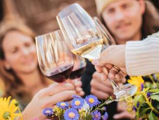 Four people are toasting with a glass of wine. There are flowers on the table.