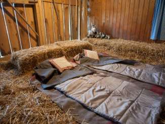 In a room lined with straw, two woolen blankets, along with pillows and other blankets, serve as a bed.