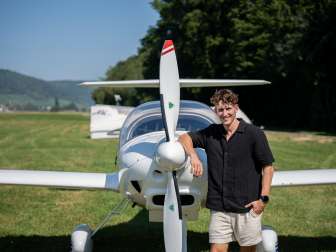 Lukas Britschgi Lukas Britschgi, European figure skating champion, leans against a glider. He is wearing a black short-sleeved shirt and beige shorts.
