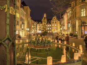 Christmas lights on Fronwagplatz in the old town of Schaffhausen. In the middle is a Christmas tree with a string of lights and there are tea lights on the Mohrenbrunnen fountain