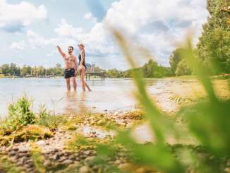 Two people in swimwear are standing on a sandy beach in the Rhine.