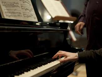 A piano with sheet music. A person plays with one hand.