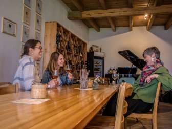 Culinary Trail Stein am Rhein Three friends are sitting at a wooden table enjoying a glass of wine. In the background is a grand piano and a wine rack.