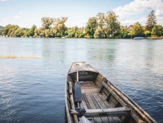 A traditional wooden boat from Schaffhausen is moored on the bank. You have a view of the Rhine and the green banks.