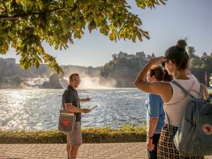 A guide stands with the group at the Rhine Falls basin and talks about the largest waterfall in Europe.