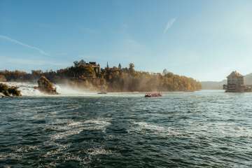 Rhine Falls in fall View of the largest waterfall in Europe. Boats sail in the basin, the trees are covered in golden autumn leaves and you can see Schloss Laufen and Schlössli Wörth.