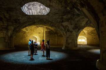 A group with a guide stands in the cash desk of the Munot. Light falls through shafts of light and forms circles on the floor.