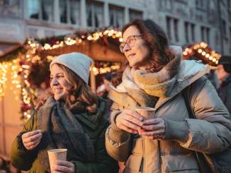 Two women with a mug of mulled wine in their hands at a Christmas market.