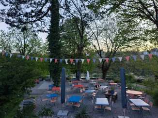 Carcajou Rhine Valley Garden Blue and red tables and chairs are set up on a terrace directly on the Rhine.