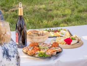 On a table with a white tablecloth outside are platters with various starters. There is a platter with cheese, one with sandwiches with toppings and one with melons.