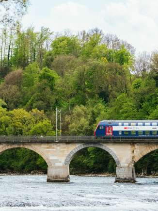rheinfall-bridge-train-april-fruehling An SBB train crosses the Rhine Falls Bridge from the right edge of the picture.