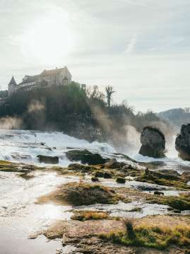 View of the two Rhine Falls rocks and Schloss Laufen from behind. The air is clear in winter and the sun is reflected in the water.
