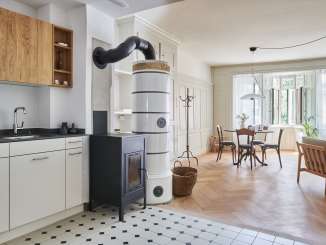 Kitchen with black and white tiles and an old oven. Dining area with herringbone wooden floor and a dining table with 4 chairs. The room is bright and flooded with light.