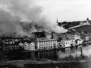 An old black and white picture of a city. Dark clouds rise over the city.