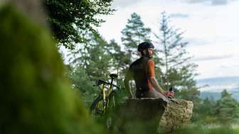 A cyclist is sitting on a large rock, taking a break during his gravel ride.