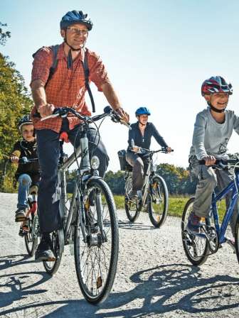 A family cycles on a dirt road, surrounded by meadows, fields, and a forest.