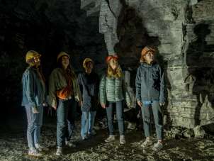 Five friends are wearing yellow and orange helmets. They are standing in a former plaster gallery.