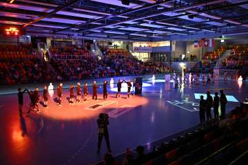 The players of a handball team stand in the middle of the hall and high-five the opposing team.
