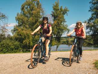 Two friends are riding their e-bikes along a lake.
