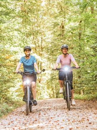 Two friends are riding their e-bikes along a nature trail through the woods.