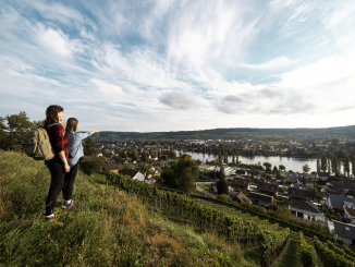 Two hikers are standing in a field above the vineyards and the town Stein am Rhein enjoying the view of the old town and the Rhine.