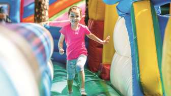 A girl is hopping and running through a bouncy castle with a smile on her face.