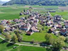 View from above of a small village surrounded by meadows, fields and wooded hills.