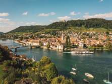 View of Stein am Rhein from the other side of the Rhine. Hohenklingen Castle can be seen on the hill and a boat passes in front of the old town.