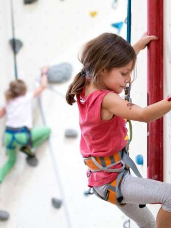 A girl climbs with a climbing harness on a climbing wall.