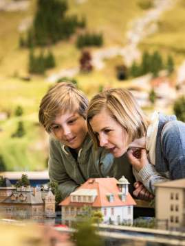 A mother is with her son in the Smilestones miniature world. They are looking at houses.