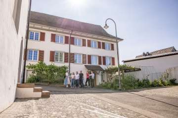 A group stands in front of a stately home. A guide in traditional costume tells us more about Hallau.