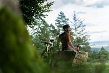 Ein Velofahrer sitz auf einem grossen Stein und macht eine Pause auf seiner Graveltour.