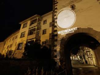 An old town facade with an archway at night. The façade is illuminated with the slogan "Museumsnacht Hegau-Schaffhausen.