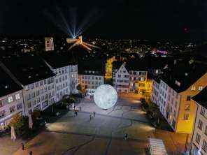 A view from above at night, showing the illuminated Munot. Beams of light shine into the night sky.