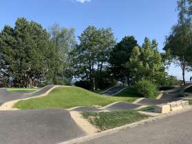 A pump track facility is surrounded by trees.