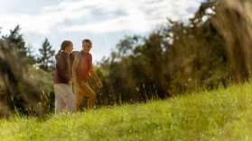A mother with a backpack is walking across a meadow with her daughter.