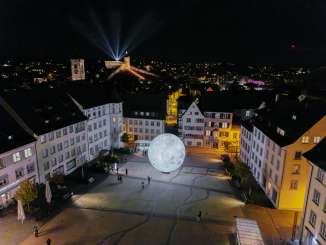 A view from above at night, showing the illuminated Munot. Beams of light shine into the night sky.