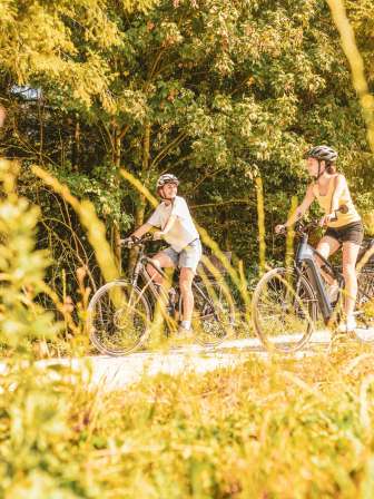 Two friends are riding their e-bikes on a dirt track at the edge of the forest.