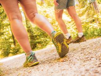 Two people are wearing hiking boots and walking along a nature trail.