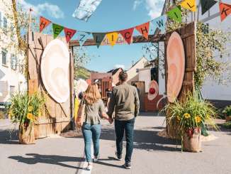 A couple holding hands. They walk through the colorfully decorated alleyways at the autumn festival in Wilchingen.