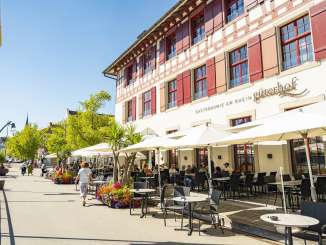 Terrace Güterhof Schaffhausen The sun terrace with a wooden platform, white parasols and tables with black chairs is located directly on a footpath along the Rhine.