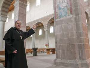 A man in a monk's costume stands in a church.