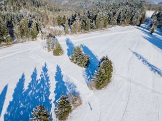 Randen cross-country ski trail View from above of the cross-country ski trail across an open area. One person is on it. There is still some snow on the fir trees.