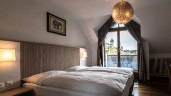 One hotel room is furnished with a double bed with white bed linen. From the window you have a view of the Munot fortress in Schaffhausen.