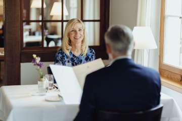 Two people are sitting at a table set with a white tablecloth and looking at the menu.