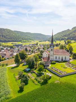 Blick von oben auf die Kirche und das Dorf Merishausen. Die Umgebung leuchtet in einem satten grün.