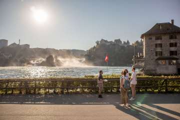 A group with a guide stand in front of the Rhine Falls, the largest waterfall in Europe.