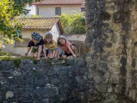 Three children squatting on a stone wall in a village.
