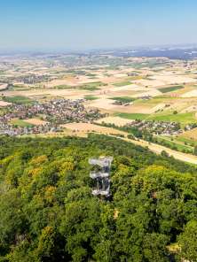 Siblingen Randenturm with village In the foreground you can see a tower rising out of the forest. In the background you can see a flat landscape with many villages and fields.